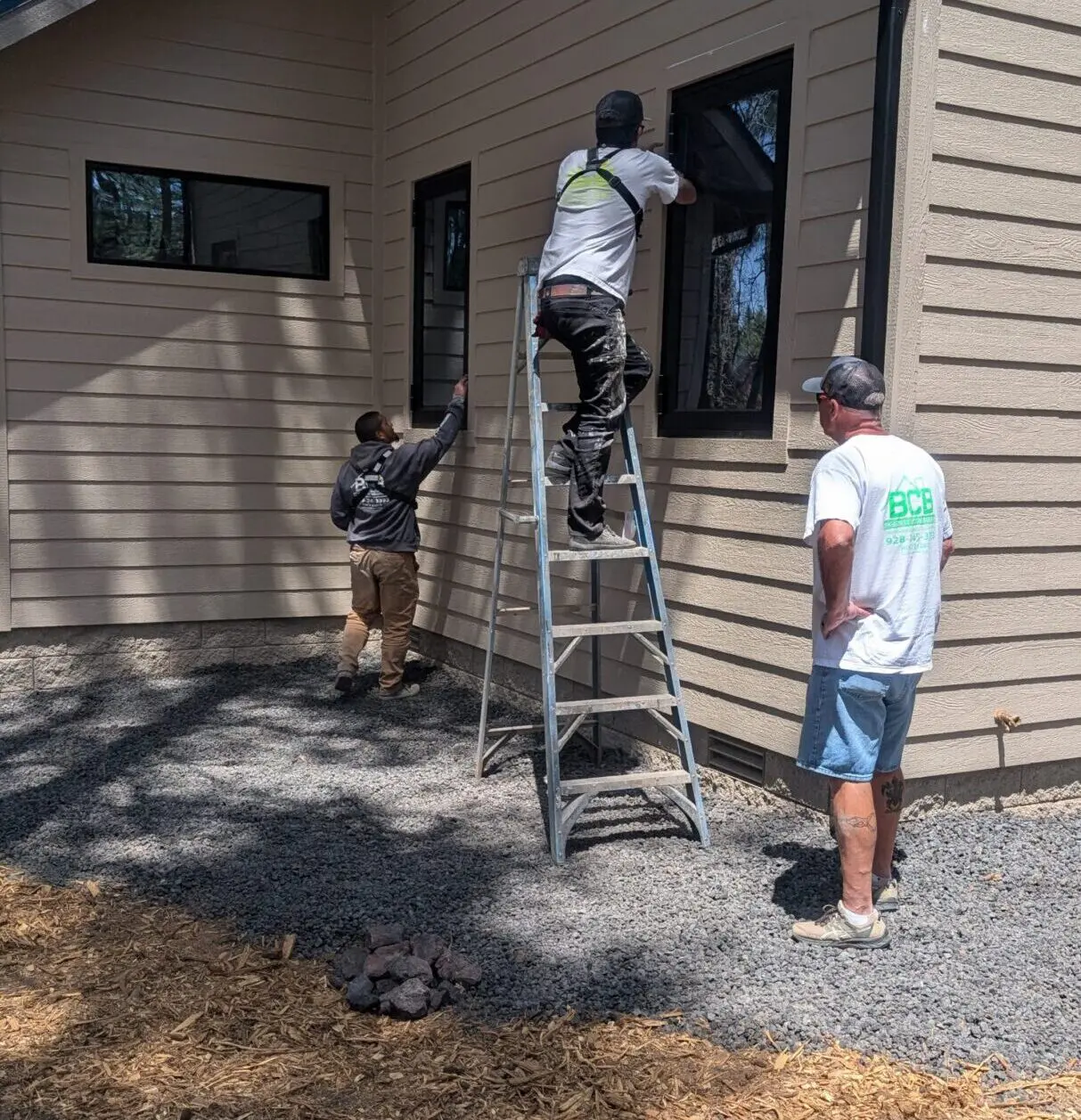 Three men working on a house exterior, one on a ladder cleaning a window.