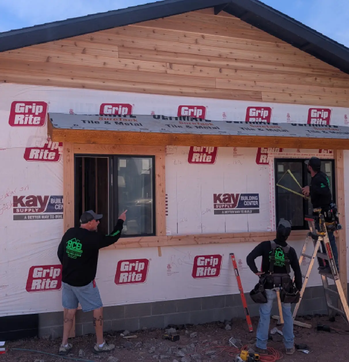 Two men installing a window on a wooden house under construction.
