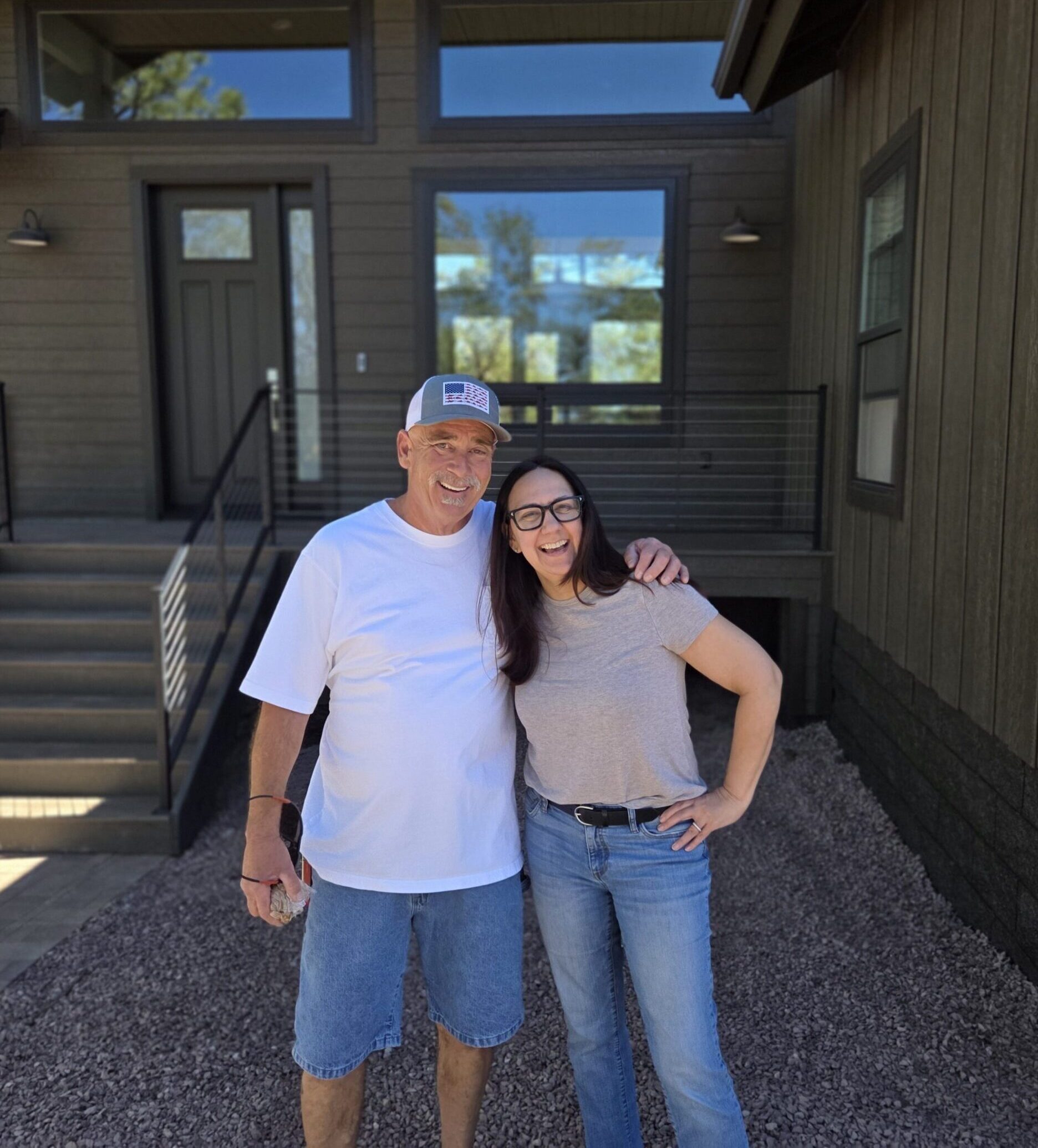 A smiling older man and young woman posing outside a house on a sunny day.